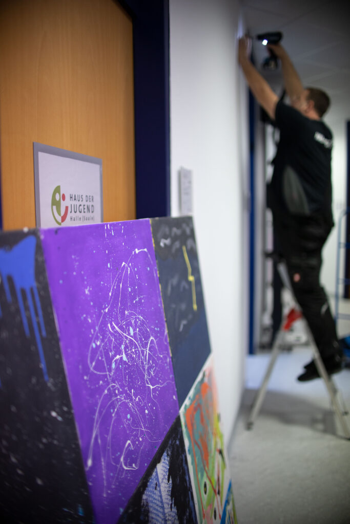 Ein Mitarbeiter steht auf einer Leiter und bringt ein Bild an die Wand
