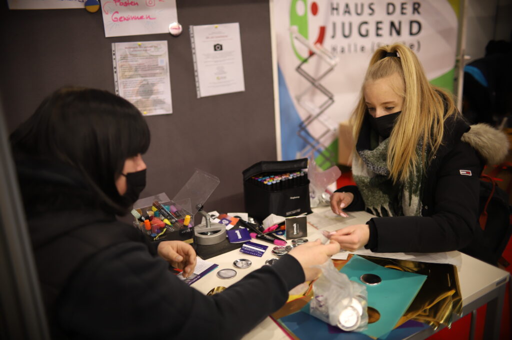 Junge Menschen basteln eigene Buttons am Stand des Hauses der Jugend