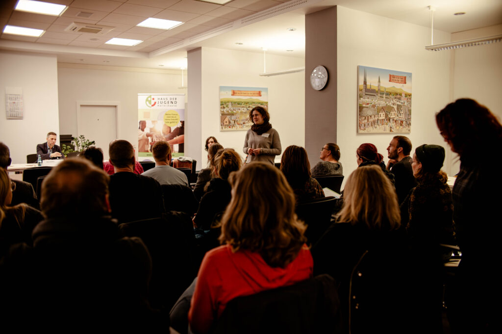 Eine Frau im Publikum spricht bei einer Konferenz des Hauses der Jugend