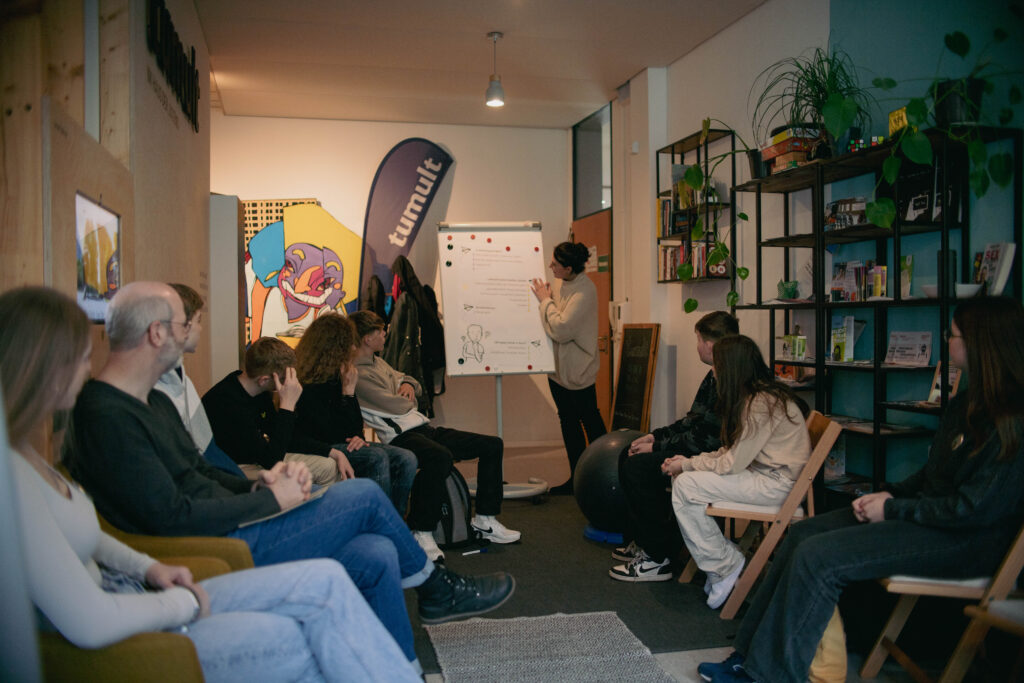 Junge Menschen sitzen im Stuhlkreis in einem Raum bei einer kurzen Vorstellung des Hauses der Jugend durch die Koordinatorin