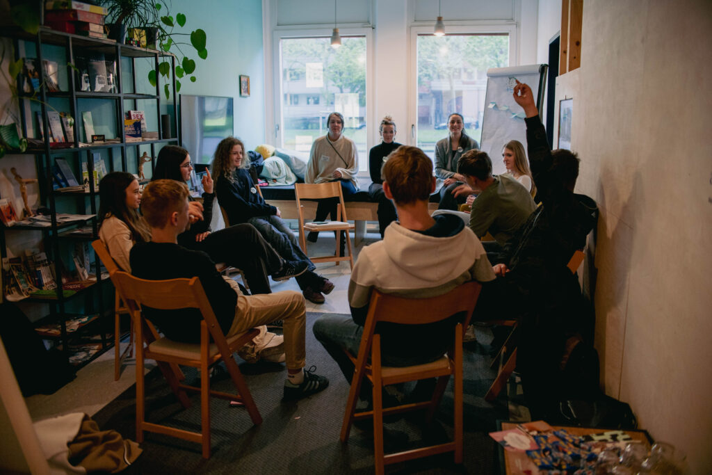 Junge Menschen sitzen im Stuhlkreis in einem Raum bei einem Workshop über Geschlechterrollen-Klischees