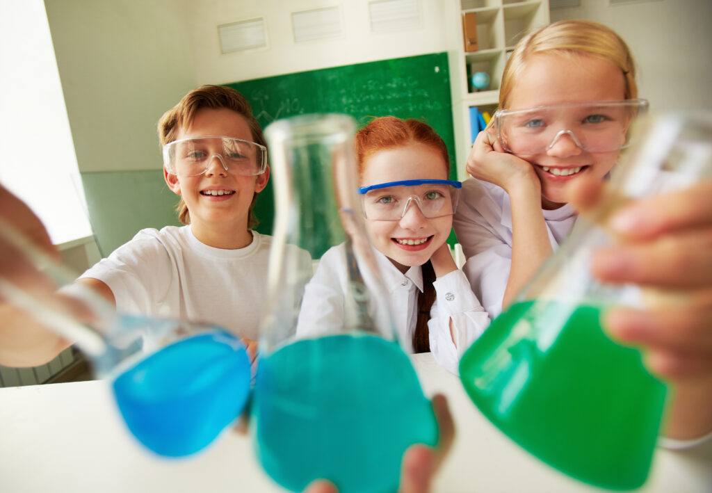 Three happy schoolchildren holding tubes with chemical liquids