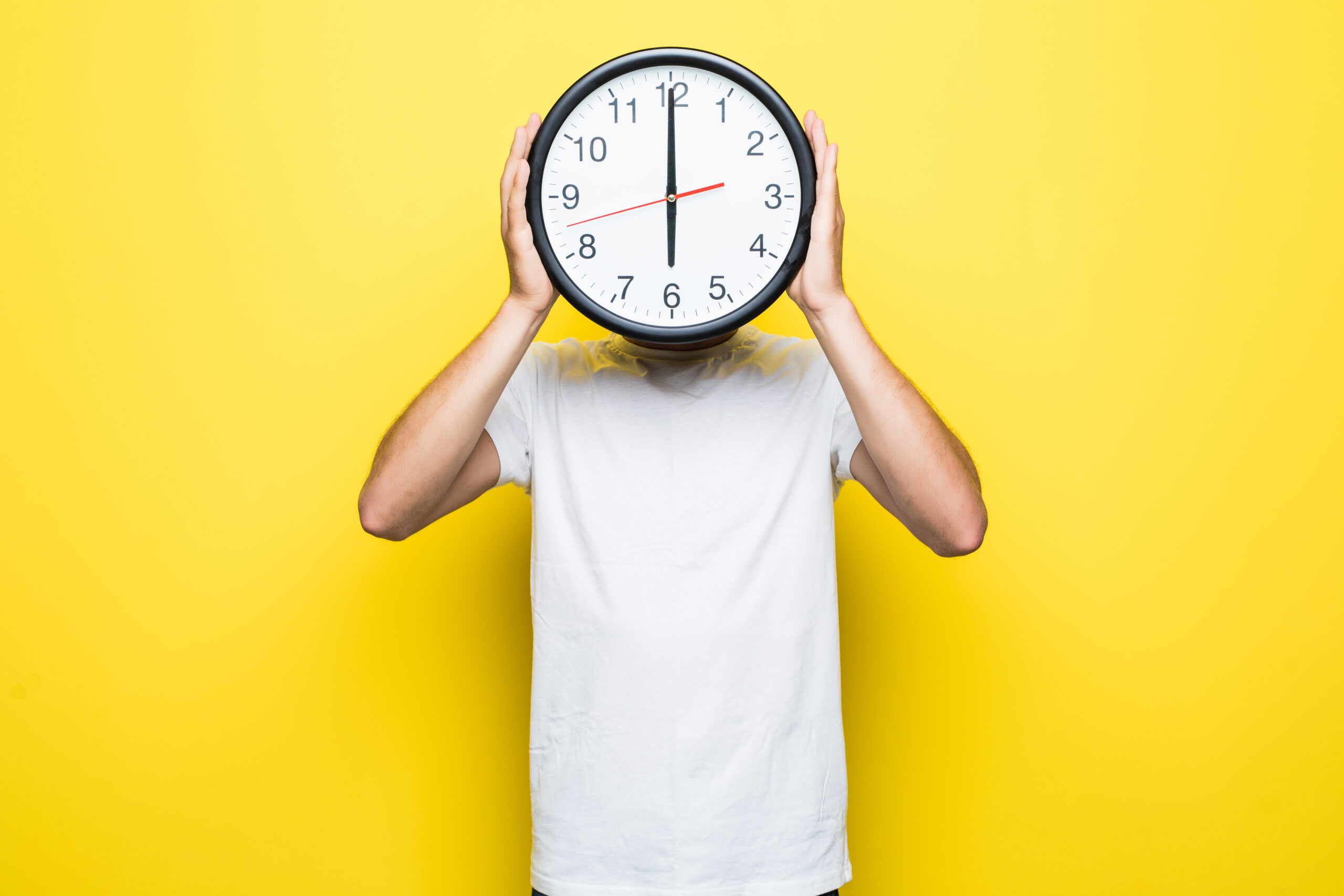 Mann hält große Uhr vor seinem Kopf mit gelben Hintergrund