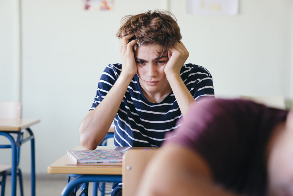 Deprimierter Schüler sitzt im Klassenzimmer und stützt Kopf auf Händen ab